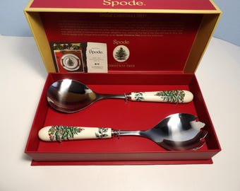 May include: A red box with a gold trim containing a set of two Spode Christmas Tree salad servers. The servers have a white handle with a green Christmas tree design and a silver metal head.