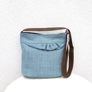 May include: A light blue canvas shoulder bag with a brown strap and a ruffle detail at the top.