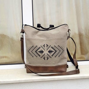 Mochila conversível em lona com estampa asteca e alça transversal em couro vegano.