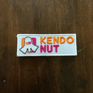 Può includere: Toppa ricamata bianca con una grafica fantasma rosa e arancione e il testo "KENDO NUT" in arancione.
