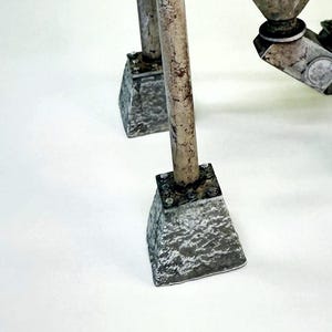 May include: A model of a metal structure with four gray concrete bases and a metal pipe with a red accent. The structure is on a white surface.