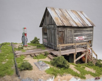 May include: A model train set with a weathered wooden shack, a gas pump, and a railroad track. The shack has a sign that reads "Danger No Smoking".