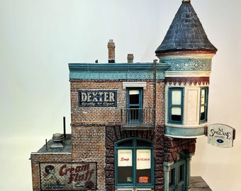 May include: A detailed model of a brick building with a corner turret. The building has several signs, including "Dexter Quality Cigar", "Cream Puff", "New Hope Soup", "Mission Kitchen", and "M. Spillane Private Detective".