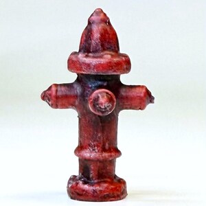 Op de afbeelding: Een rode brandkraan miniatuur, gemaakt van geverfd hars, met een gedetailleerd ontwerp. De brandkraan heeft een afgeronde bovenkant en een kruisvormige basis.