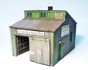 May include: A model of a rusty metal building with green trim. The building has a sign that reads "Aultman Miller Machine Shop & Welding".