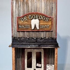 May include: A wooden storefront with a sign that reads "Dr. Gordon Painless Dentist". The storefront has a large tooth on the sign and a smaller sign that reads "Dr. Lyon's Tooth Powder".