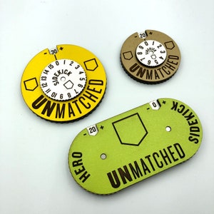 May include: Three circular game pieces with a yellow, green, and brown background. Each piece has a white circle with black text that reads "Sidekick" and "Unmatched".