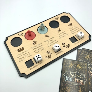 May include: A wooden game board with black accents and engraved text. The board features two player sections with dice, miniature figures, and spaces for cards. The text on the board includes "Player 1 VP", "Player 2 VP", "Round", "Draw 2 Tactic & Place 1 Condition on Enemy Unit", "1 Enemy Unit Must Make a Panic Test & Suffers -1 Roll", "Restore Up to 3 Wounds & 1 Condition from 1 Unit", "1 Unit May Make a Free Attack Action", "1 Unit May Make a Free Maneuver or Retreat Action". The board is part of a tabletop miniatures game called "A Song of Ice & Fire".