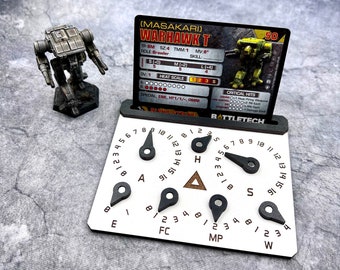 May include: A white plastic game board with a black and white mech miniature on a card. The card has the text "(MASAKARI) WARHAWK T" and "BATTLETECH". The board has dials for movement, heat, and other game stats.
