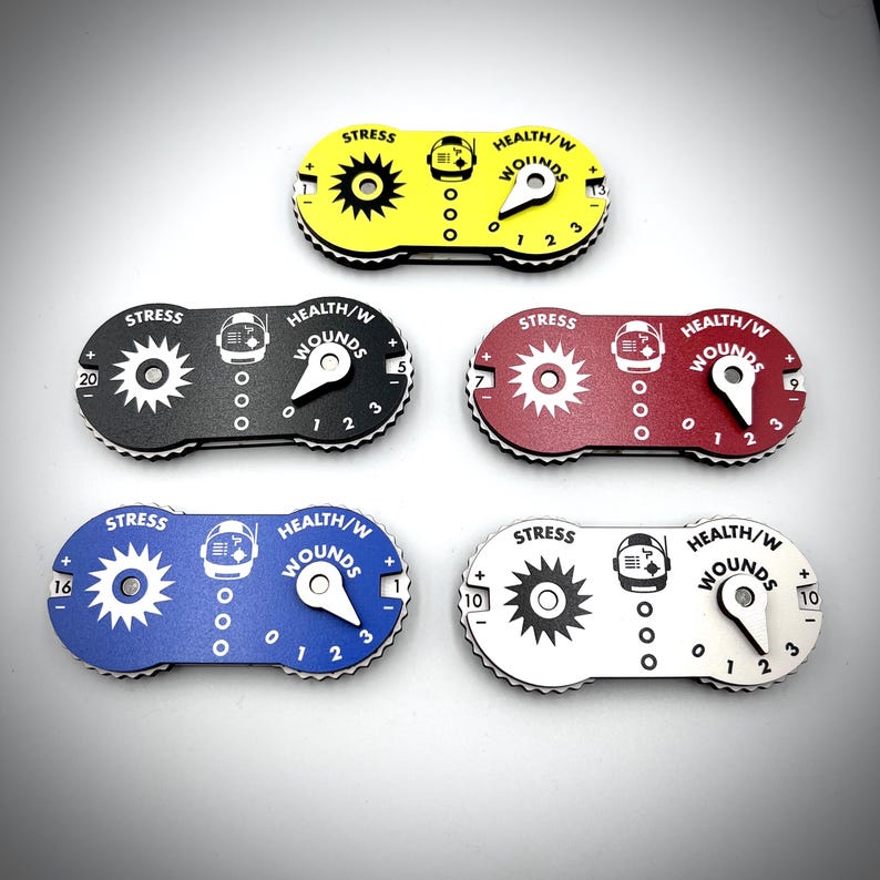 Puede incluir: Cinco rastreadores de juego ovalados en amarillo, negro, rojo, azul y blanco. Cada uno presenta un dial de estr&eacute;s en forma de engranaje, un dial de salud y heridas con puntero, y un icono de casco de astronauta con el texto STRESS y HEALTH/W WOUNDS.