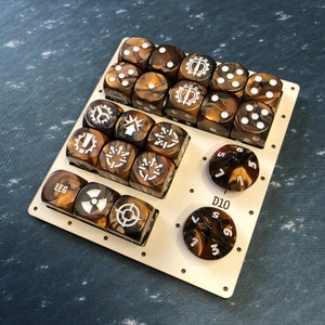 May include: A wooden game tray with a set of dice. The dice are brown and gold with white markings. The tray has a D10, a D6, and a LEG label.