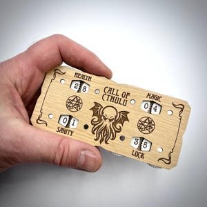 May include: A wooden Call of Cthulhu character tracker with dials for Health, Sanity, Luck, and Magic. The dials are set to 28, 01, 35, and 04 respectively. The tracker features a stylised image of Cthulhu.