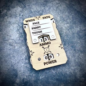 May include: A wooden game tracker with a sliding white panel. The tracker has labels for WNDS, PACE, PARRY, and TOUGH. It also displays AMMO and POWER values. The design includes a shield and arrow graphic and starburst details.