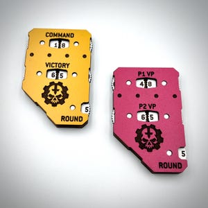 May include: Two wooden game tokens, one yellow and one pink, with engraved text and symbols. The yellow token reads "COMMAND", "VICTORY", and "ROUND", with a skull and gear emblem. The pink token reads "P1 VP", "P2 VP", and "ROUND".