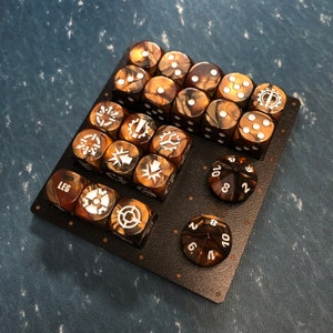 May include: A set of 20 brown and gold dice with white markings. The dice are arranged in a grid pattern on a black surface. The dice have different symbols and numbers on each side.