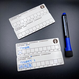 May include: Two silver metal cards with a sword icon and a grid of numbers from 1 to 10. The cards are labeled "Troublesome", "Extreme", "Epic", "Dangerous", and "Formidable". The top card has a blue marker on it. The bottom card has the words "Timer" and "Quest I" written on it.