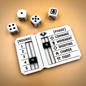 May include: A white board game tracker with black text and icons. The tracker has a round counter with numbers 1 through 5 and a phase counter with the words "Command", "Movement", "Shooting", "Charge", and "Fight". There are five white dice with black dots on a beige surface.
