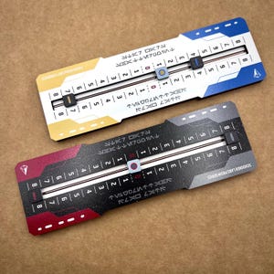 Puede incluir: Dos contadores de juego rectangulares de la serie Schooner Labs Prism. El contador superior es blanco con detalles en azul y amarillo, con marcadores deslizantes y números del 0 al 8. El contador inferior es negro con detalles en rojo y gris, también con marcadores deslizantes y números del 0 al 8. Ambos incluyen texto y símbolos estilizados.