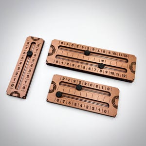 May include: Three wooden number sliders with black knobs. One slider is vertical, displaying numbers 0-8. The other two are horizontal, with numbers 0-12 and 0-8. The wood has a reddish-brown hue.