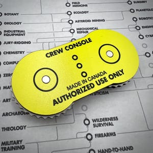 Puede incluir: Una insignia de color amarillo brillante en forma de p&iacute;ldora con el texto en negro CREW CONSOLE, MADE IN CANADA y AUTHORIZED USE ONLY. El dise&ntilde;o incluye dos iconos circulares negros y tres puntos verticales centrados.