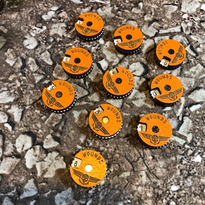 May include: Ten orange and brown circular wound counters with a skull and wings design. Each counter has a number from 0 to 9 printed on it.