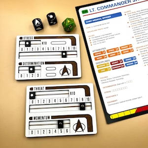May include: A set of wooden character sheets for a tabletop role-playing game. The sheets feature a Star Trek theme and include stats for stress, determination, threat, and momentum. The character sheet also includes a title, "Lt. Commander, Chief Medical Officer", and a description of the character's attributes, disciplines, and focuses.