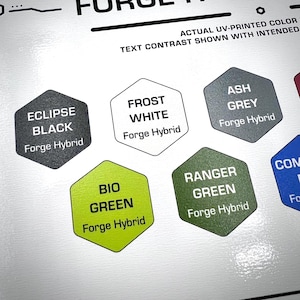 Puede incluir: Una tabla de muestras de color con iconos hexagonales etiquetados como Eclipse Black, Frost White, Ash Grey, Bio Green y Ranger Green, cada uno con el texto Forge Hybrid. La tabla incluye texto de encabezado sobre el contraste de color.