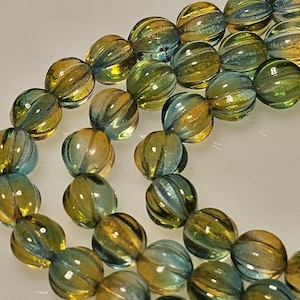 May include: Strands of glass beads in shades of yellow, green, and blue. The beads are round with a ribbed texture, creating a striped effect. The beads are strung together, likely for jewelry making or crafting.