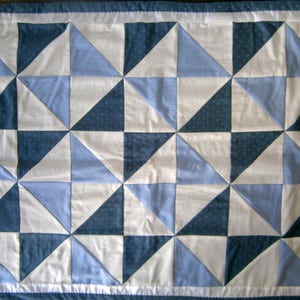 Può includere: Un trapunta bianca con un motivo a quadri blu e bianchi. La trapunta è composta da una serie di triangoli che creano un disegno geometrico.