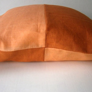 Peut inclure: Un grand coussin rectangulaire avec un design bicolore. Un côté est de couleur orange clair, tandis que l'autre côté est de couleur orange foncé. Le coussin est fait d'un tissu doux et texturé.