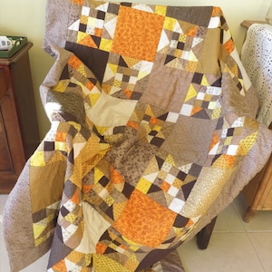 Könnte beinhalten: Eine braune, gelbe und weiße Patchwork-Decke mit Sternenmuster. Die Decke ist gefaltet und über einen Stuhl gelegt.