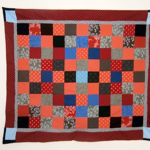 Peut inclure: Une courtepointe en patchwork avec un motif rouge, blanc et bleu. La courtepointe est composée de carrés de tissus différents, chacun avec un motif unique. La courtepointe est bordée d'un tissu rouge à pois blancs.