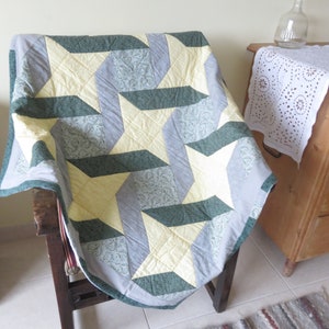 Peut inclure: Une courtepointe avec un motif géométrique d'étoiles dans des tons de vert, jaune et gris. La courtepointe est pliée et drapée sur une chaise en bois.