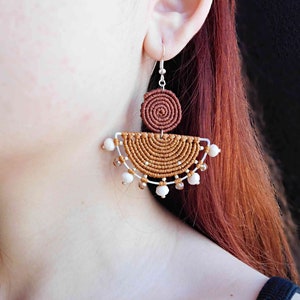 May include: A pair of brown and white macrame earrings with white beads and a silver hook.