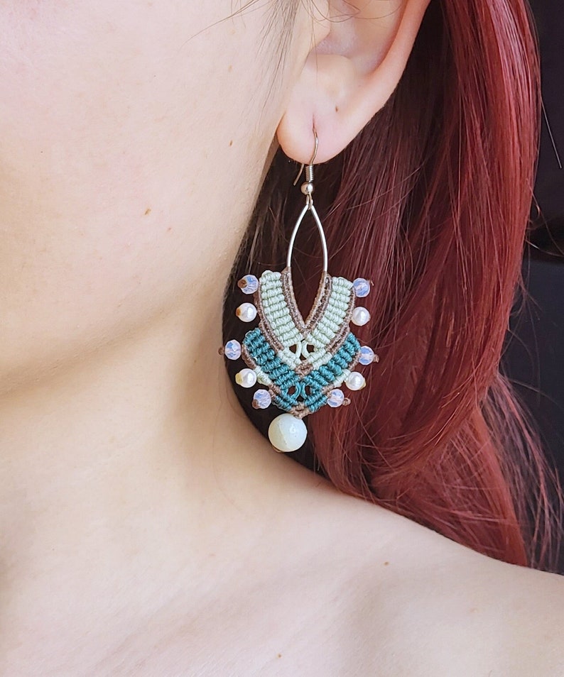 May include: A pair of green, brown, and white macrame earrings with a white stone pendant. The earrings are made with a variety of beads and have a delicate, bohemian style.