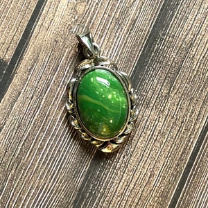 May include: A silver pendant with a green oval stone set in a decorative frame.