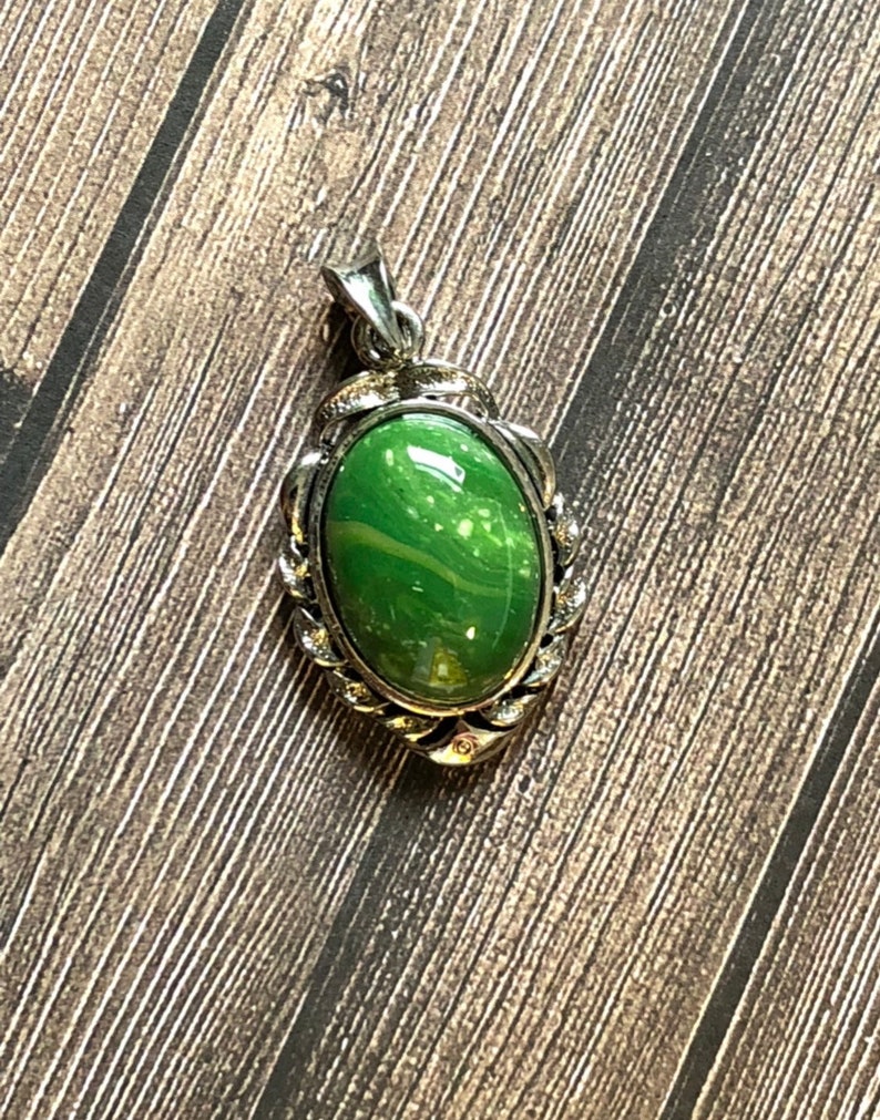 May include: A silver pendant with a green oval stone set in a decorative frame.