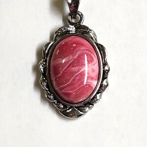 May include: A silver pendant with a pink and white oval stone set in a twisted rope design.