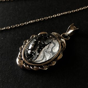 May include: A silver chain necklace with a pendant featuring a black and white marbled design encased in a silver frame.