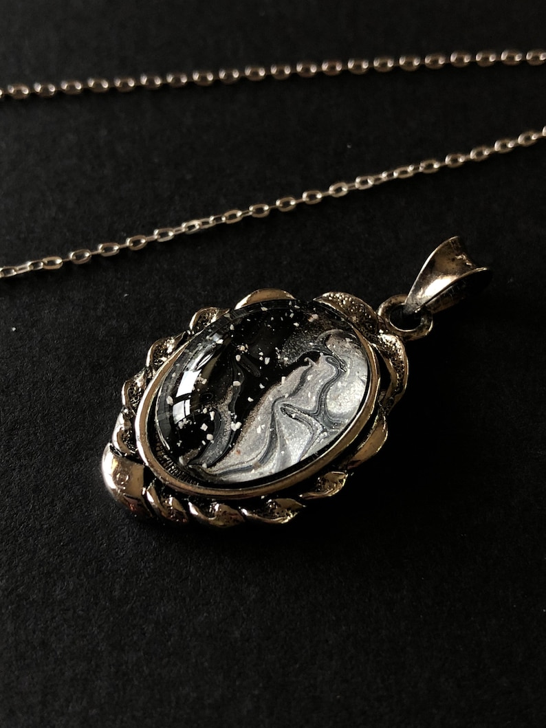 May include: A silver chain necklace with a pendant featuring a black and white marbled design encased in a silver frame.