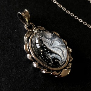 May include: A silver pendant necklace with a black and white marbled oval-shaped stone set in a silver frame.