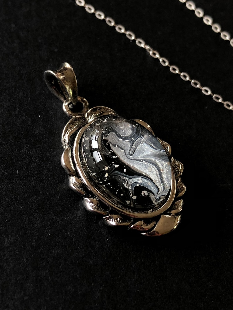 May include: A silver pendant necklace with a black and white marbled oval-shaped stone set in a silver frame.