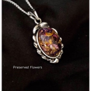 May include: A silver chain necklace with a pendant featuring a clear oval resin filled with preserved flowers in shades of pink, purple, and yellow.