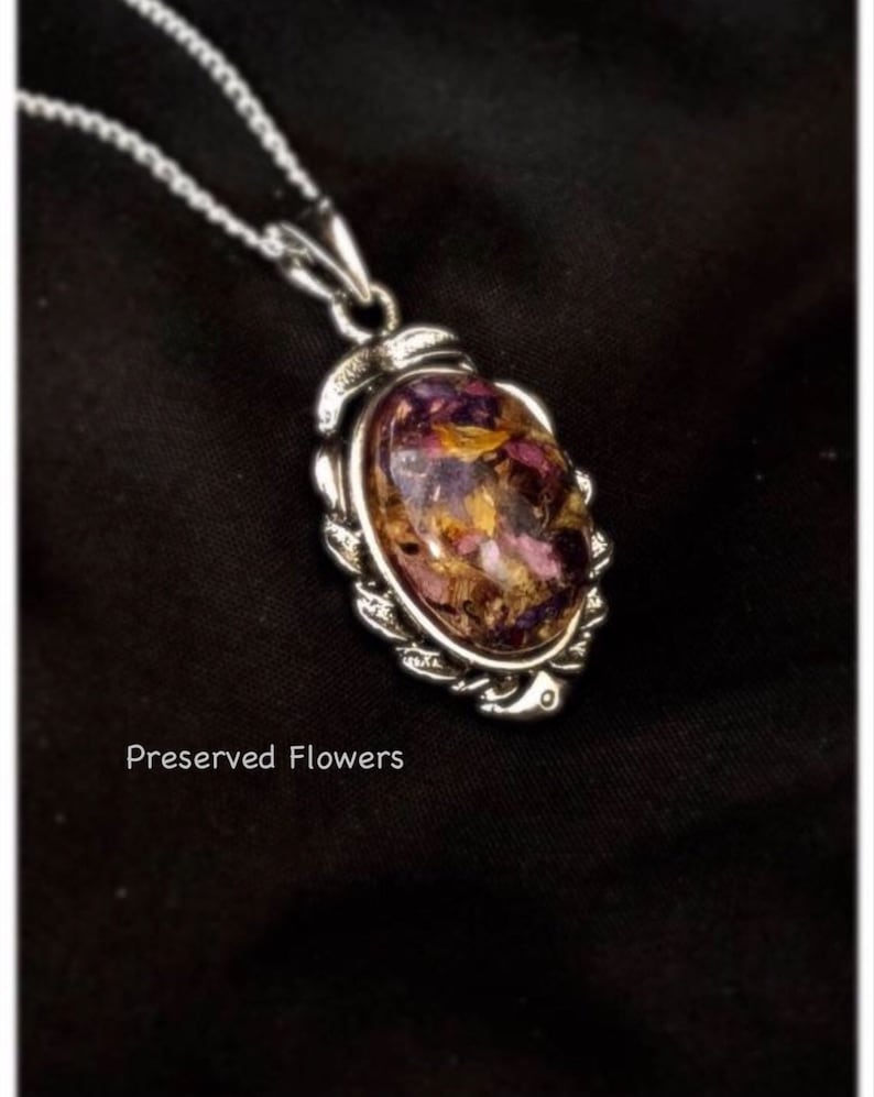 May include: A silver chain necklace with a pendant featuring a clear oval resin filled with preserved flowers in shades of pink, purple, and yellow.