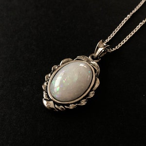 May include: A silver chain necklace with a white opal pendant. The pendant is set in a silver frame with a decorative design.