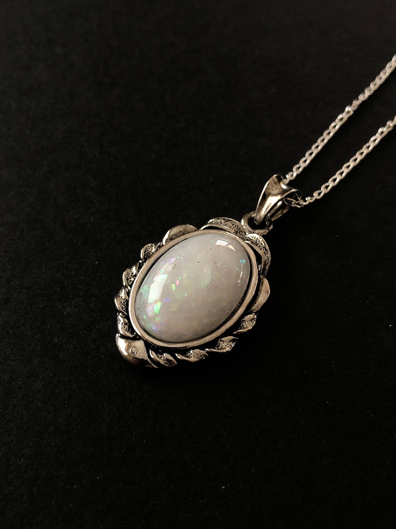 May include: A silver chain necklace with a white opal pendant. The pendant is set in a silver frame with a decorative design.