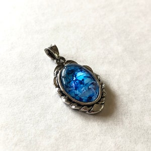 May include: A silver pendant with a blue and white marbled glass oval inlay. The pendant has a decorative, twisted rope border.