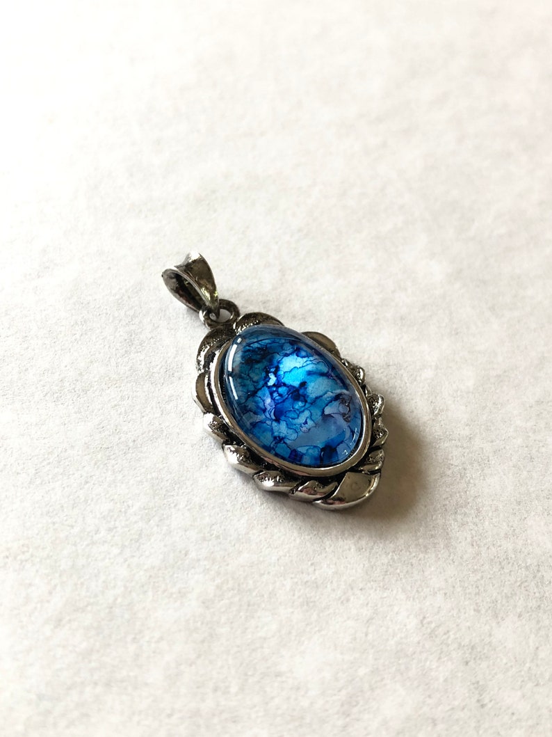 May include: A silver pendant with a blue and white marbled glass oval inlay. The pendant has a decorative, twisted rope border.
