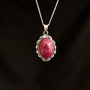 May include: A silver chain necklace with a pink oval gemstone pendant set in a silver filigree frame.