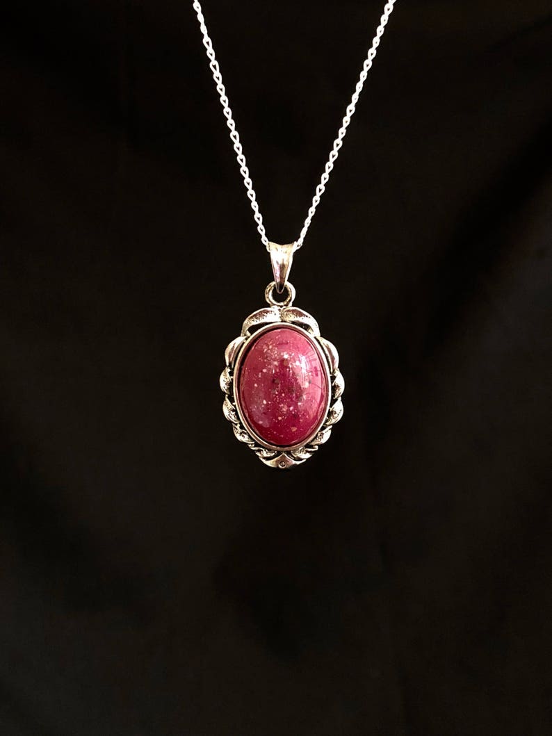 May include: A silver chain necklace with a pink oval gemstone pendant set in a silver filigree frame.